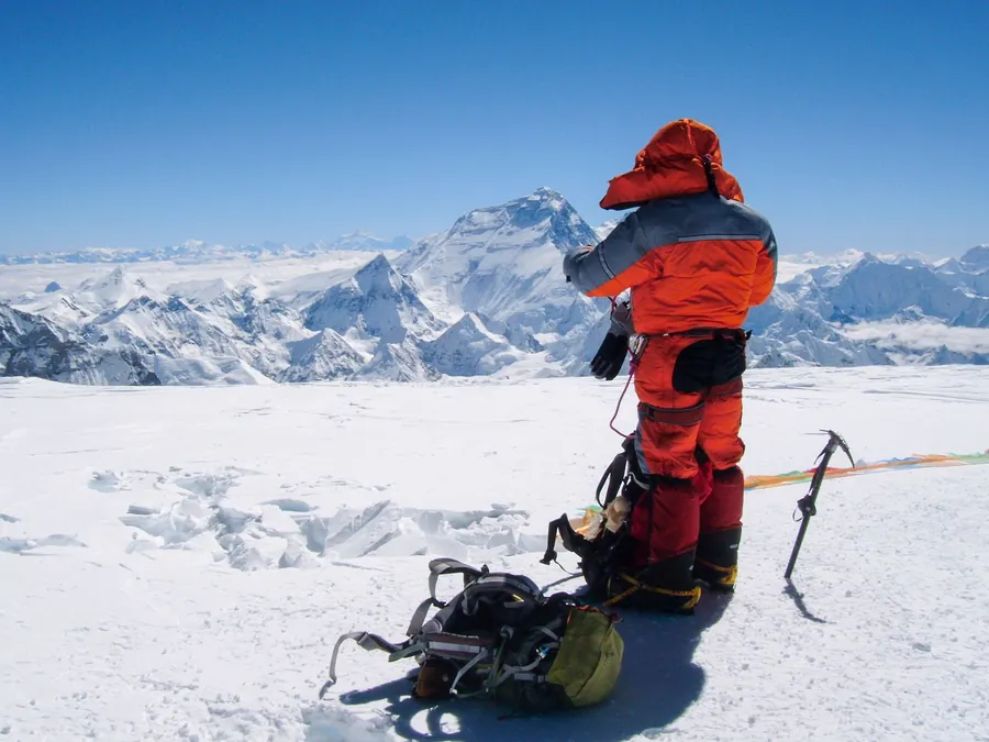 Climber in a high-altitude summit suit looking out over the Himalaya toward Everest