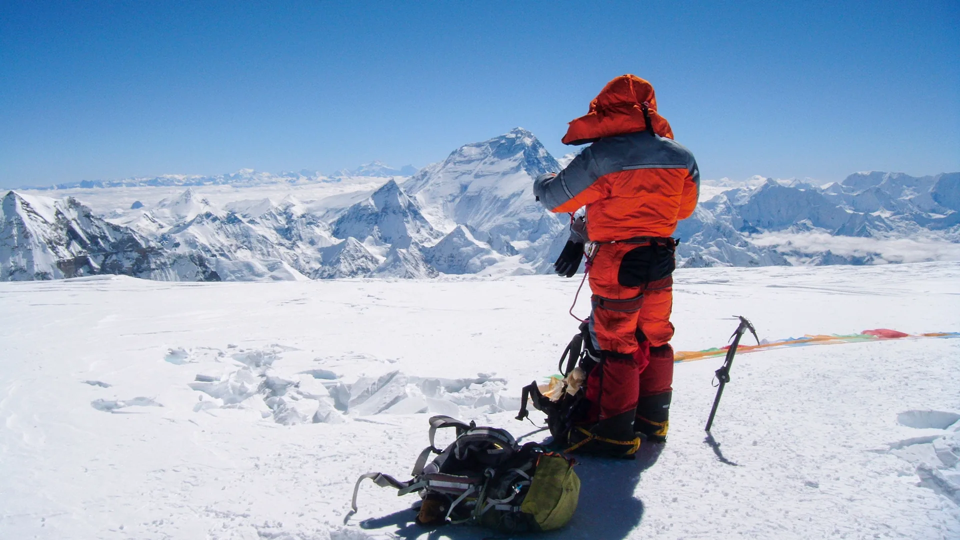 Climber in a high-altitude summit suit looking out over the Himalaya toward Everest
