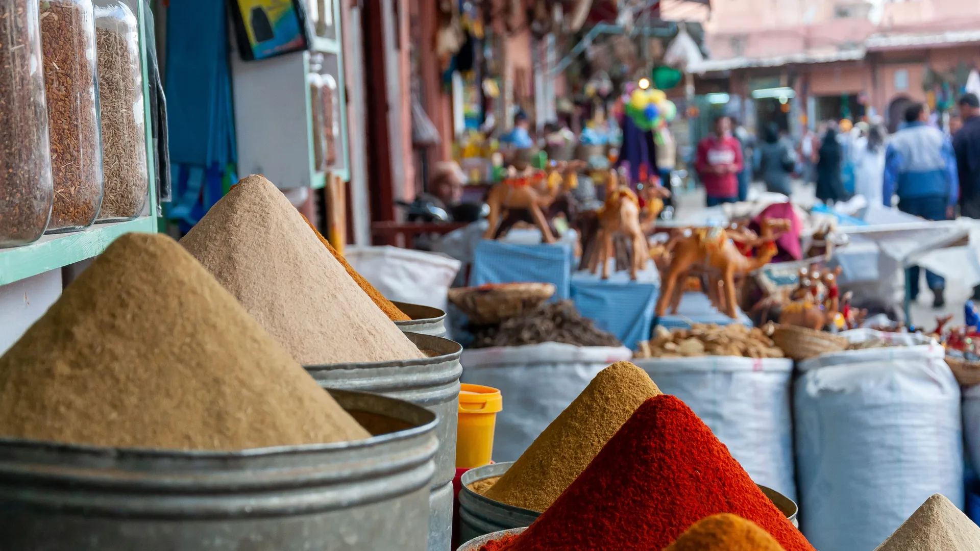 Spice stalls in a Marrakech souk, with camel figurines and shoppers in the background