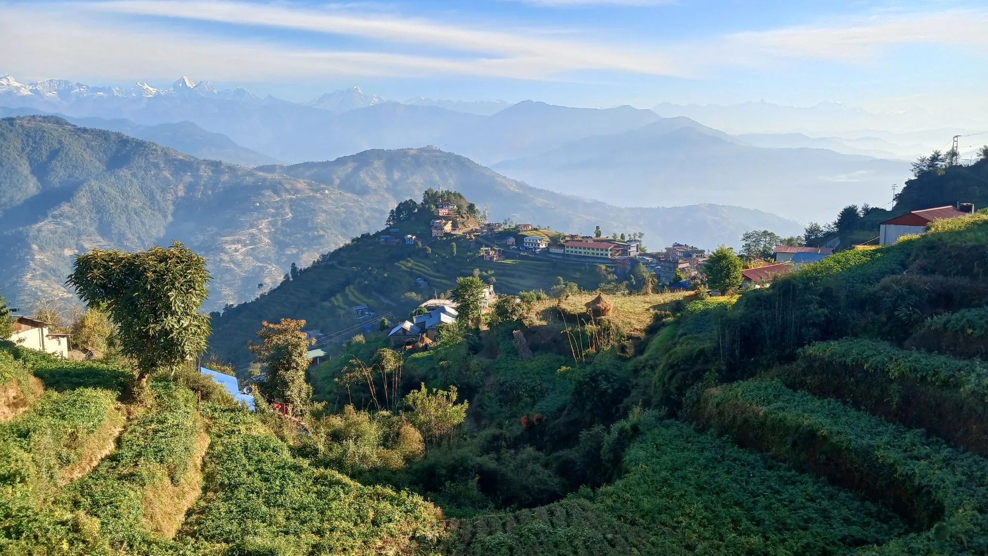 Terraced hill village in the Nepal Himalaya foothills, with snow-capped peaks on the horizon